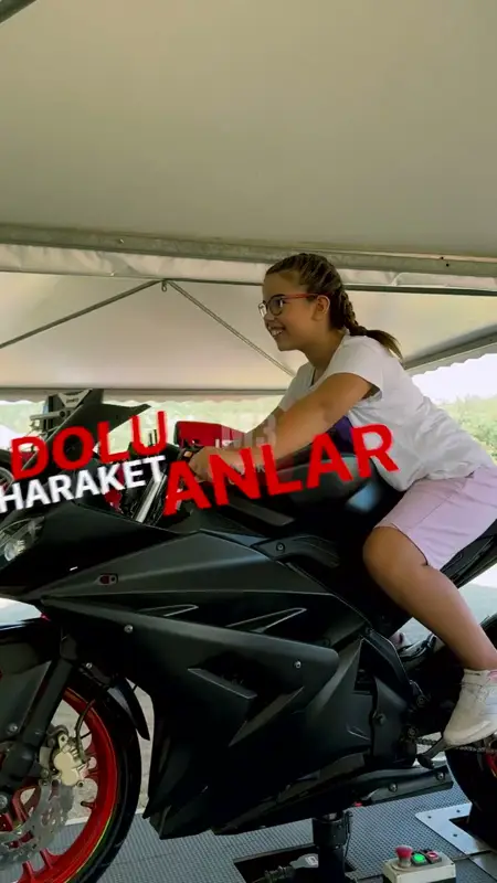 Çadır altında motosiklet simülatörüne binen gözlüklü kız çocuğu