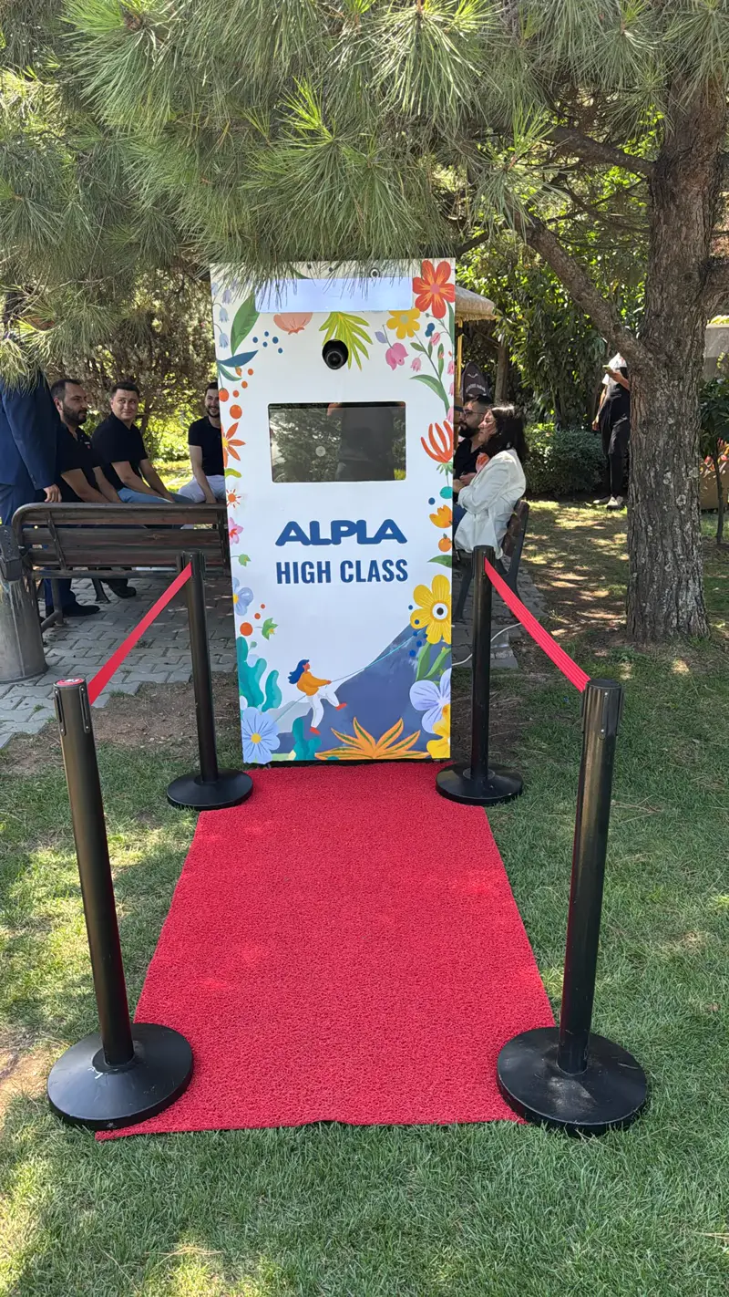 Bahçede kırmızı halı ve bariyerlerle kurulmuş ALPLA High Class markalı photo booth
