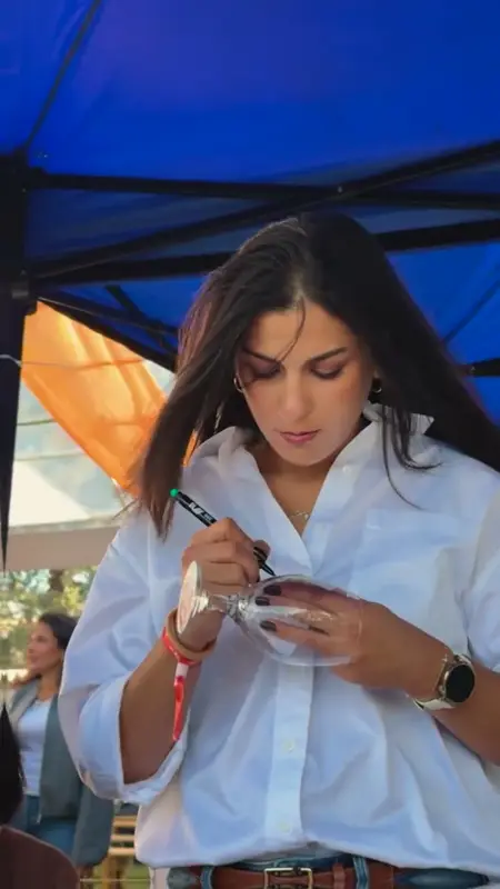 Gölgelik altında ayaklı cam bardağa kalemle desen çizen katılımcı