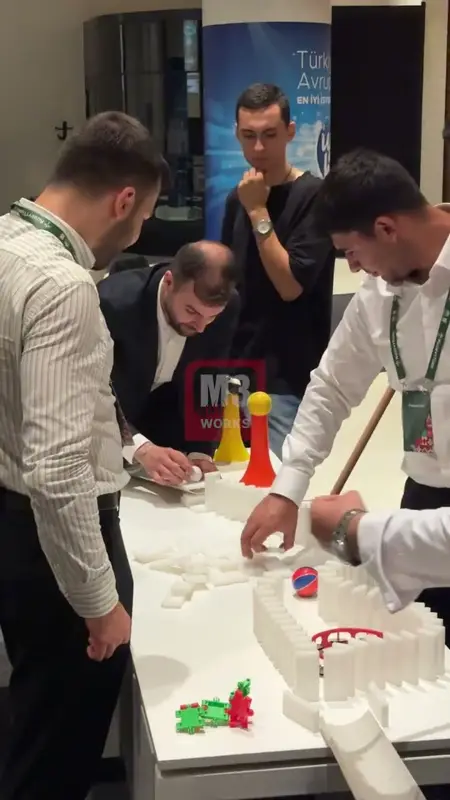 Uzun masada domino taşları, lobutlar ve toptan oluşan zincirleme reaksiyon düzeneği kuran katılımcılar