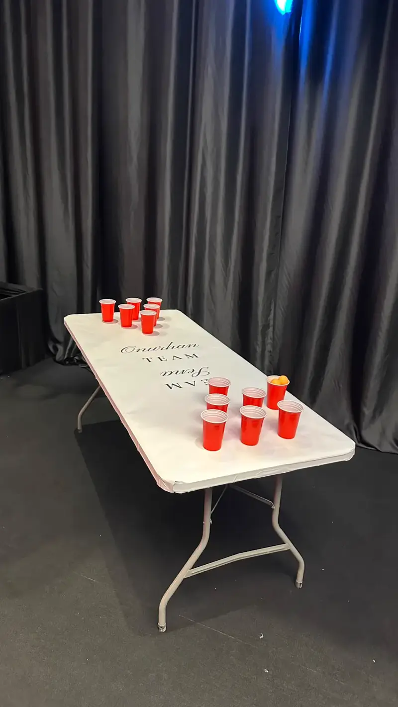 Takım isimleri yazılı beyaz beer pong masası ve kırmızı bardaklar