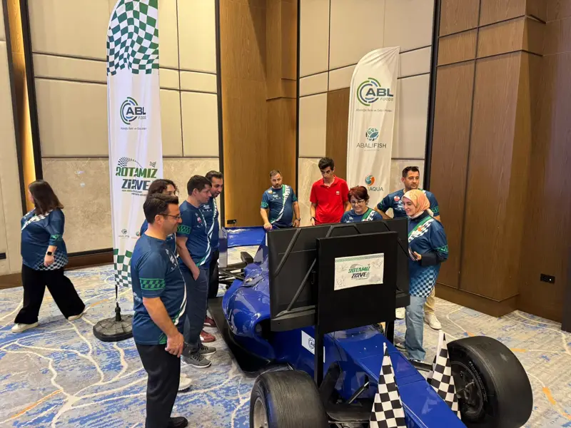 Mavi F1 simülatörünün ekranı başında toplanmış takım formalı katılımcılar