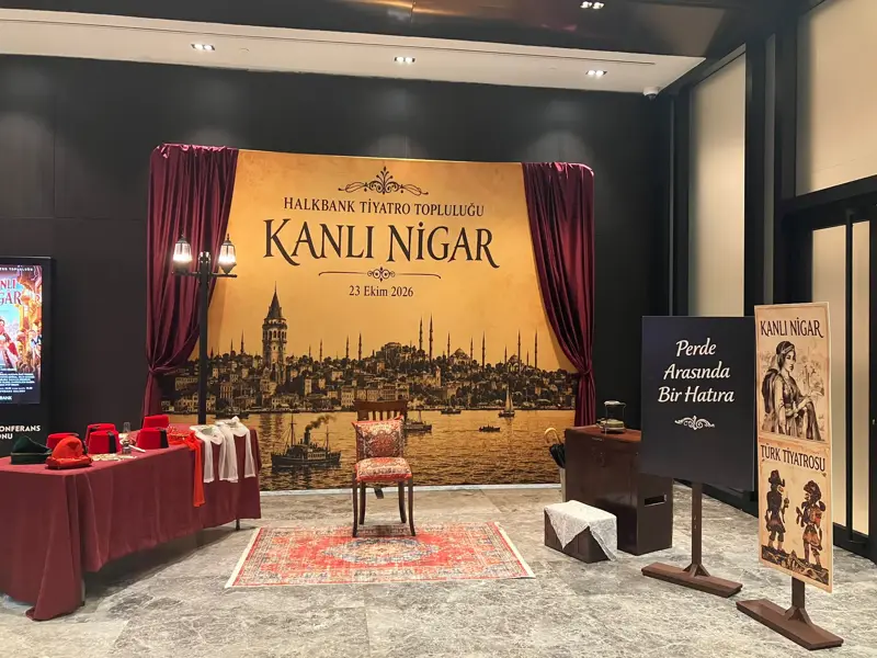 Kanlı Nigar yazılı eski İstanbul silüetli fon, kırmızı perdeler, halı, sandalye ve fes dolu aksesuar masası