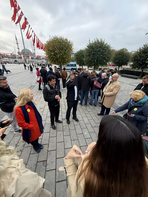 Taksim Meydanı'nda Türk bayrakları altında brifing için toplanmış Hexagon ekibi, arkada Taksim Camii