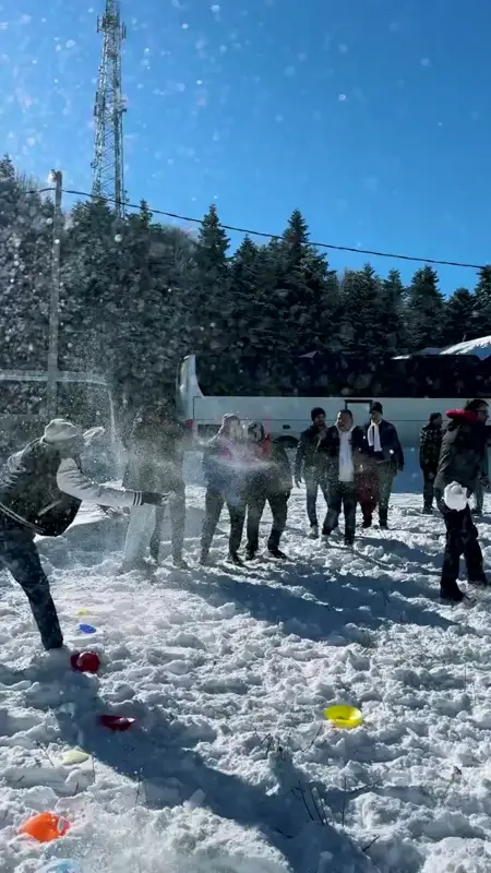 Karlı alanda renkli işaretler arasında kar topu atan takımlar ve havada uçuşan kar