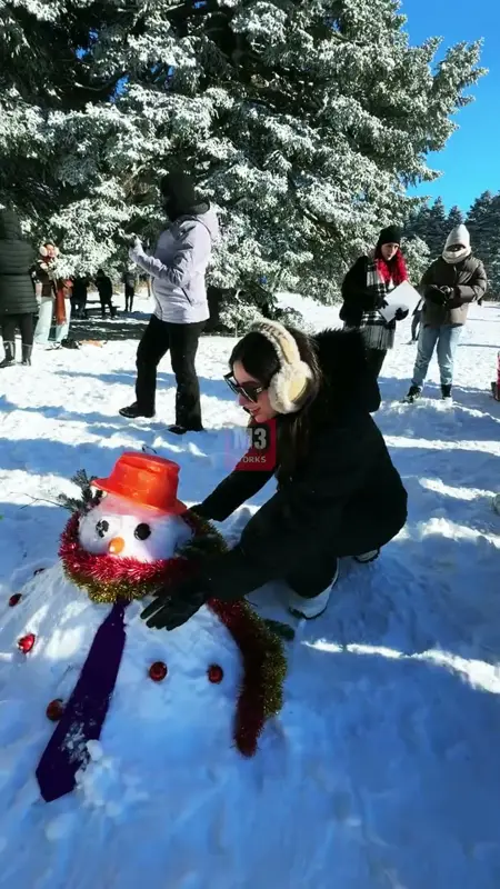 Turuncu kova şapkalı, simli süslü ve kravatlı kardan adamı tamamlayan katılımcı