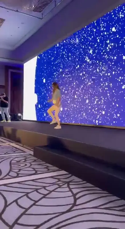 Kongre salonu sahnesinde dev LED ekranın önünde zumba hareketi gösteren dans eğitmeni