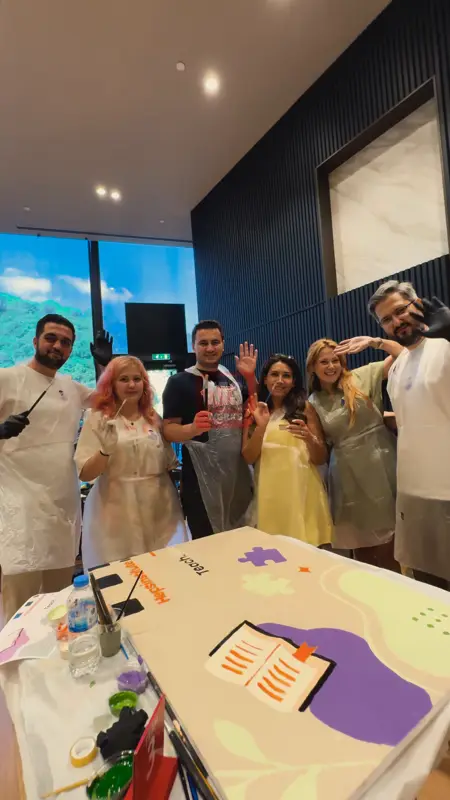 Önlüklü katılımcıların boyadıkları tuvalin başında verdikleri grup pozu