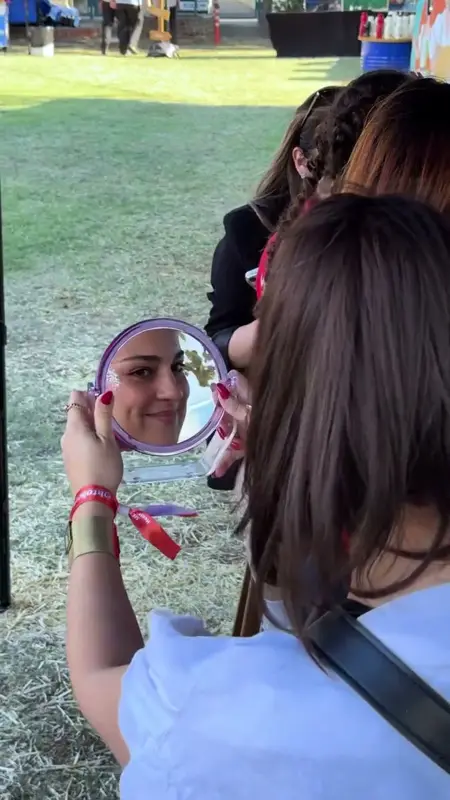 A smiling participant checking her glitter makeup in a hand mirror
