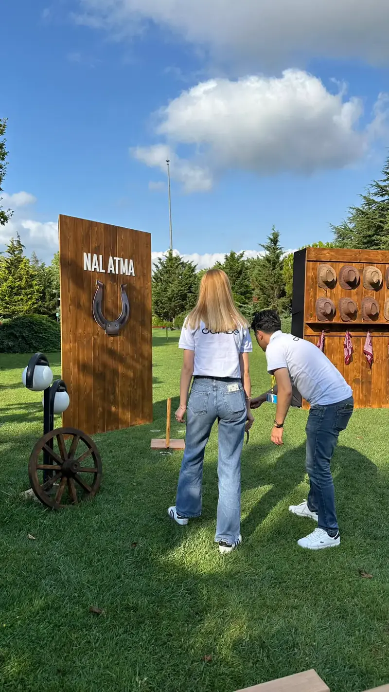 Nal atma oynayan katılımcılar ve arkada şapka asma panosu