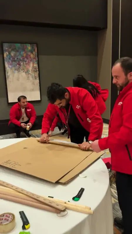 A team measuring wooden sticks and marking cardboard at a table