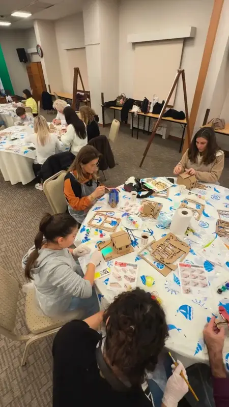 Mavi desenli masa örtülü masalarda ahşap oyuncak parçalarını boyayan çocuklar ve yetişkinler