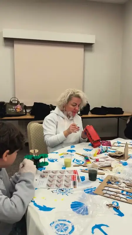 Kırmızı ahşap otobüs ve yeşil ağaç figürünü boyayan yetişkin ve çocuk