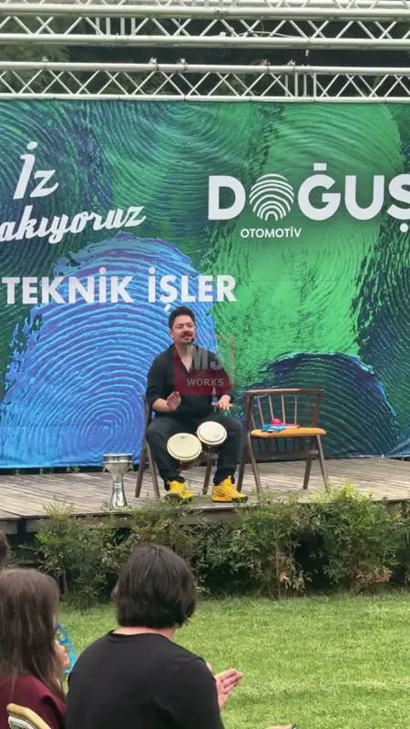 Rhythm facilitator playing percussion on an outdoor stage with participants watching from the lawn