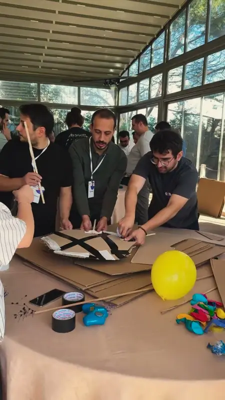 Takım üyeleri masada karton gövdeyi bantla sabitliyor, yanında balon ve bant ruloları