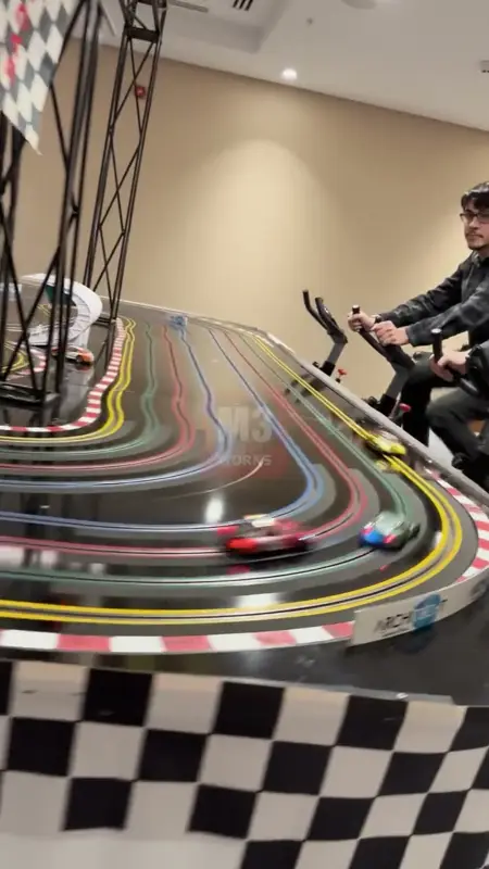 Damalı kaplamalı slot car pisti ve yanında kondisyon bisikletindeki yarışçı
