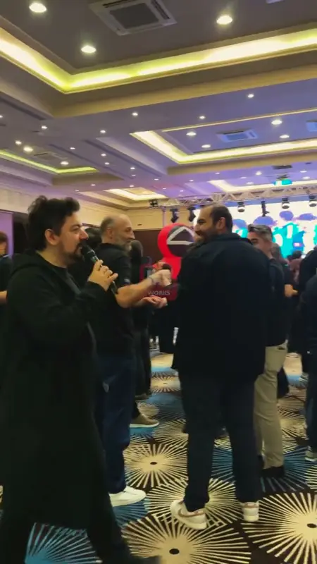 Balo salonunda mikrofonlu sunucu ve oyun öncesi toplanan katılımcılar