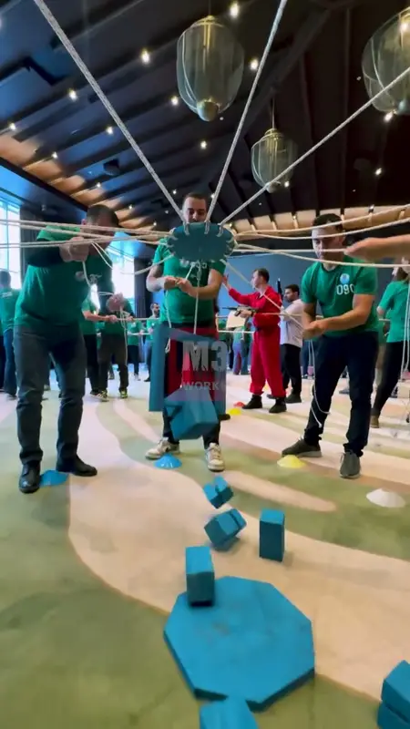 Participants in green shirts moving blue blocks with ropes in a coordination game