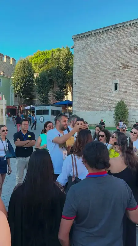 Tarihi taş surun önünde görevlinin etrafında toplanan katılımcılar