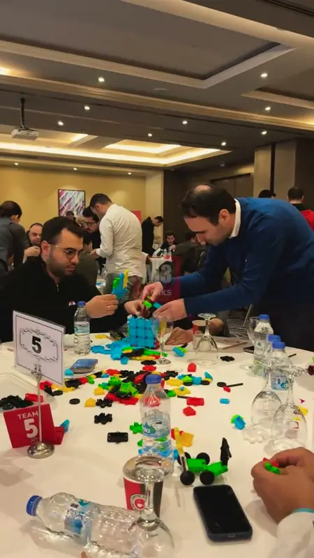 Yuvarlak masada renkli plastik parçalarla maket kuran takım üyeleri