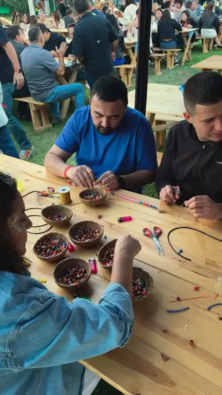 Bahçedeki ahşap masada boncuk ve kordonlarla çalışan iki katılımcı