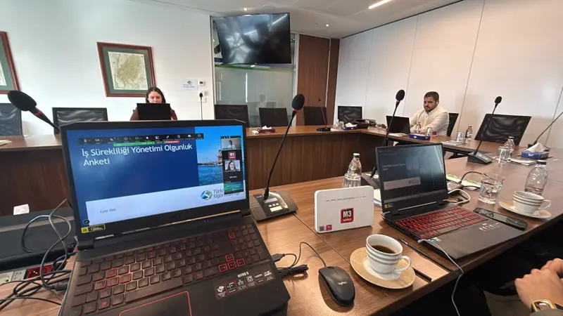 Laptop showing the Business Continuity Management Maturity Survey presentation on a meeting table with microphones and an M3 Works streaming device